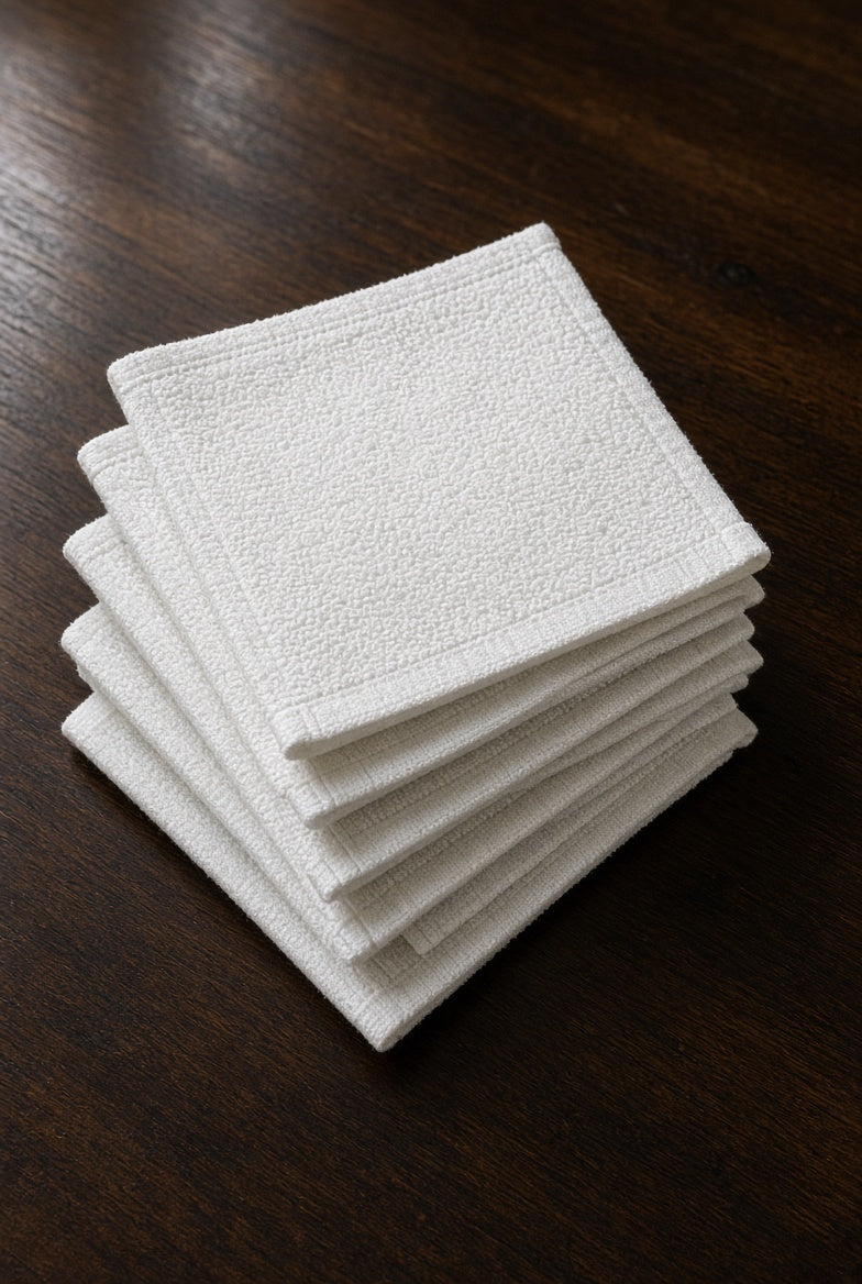 Five White Washcloths stacked in a fan on a dark wooden table, showing the hemmed edges